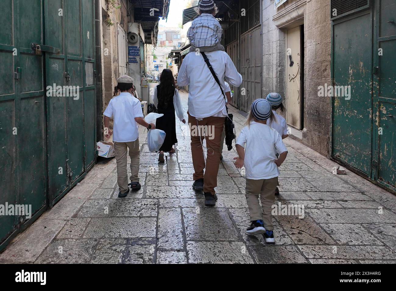 Un colon juif religieux avec un fusil d'assaut dans le dos, marche avec ses enfants via le quartier musulman pendant les vacances de Pessah juive (Pâque) dans la vieille ville le 24 avril 2024 à Jérusalem. Israël Banque D'Images