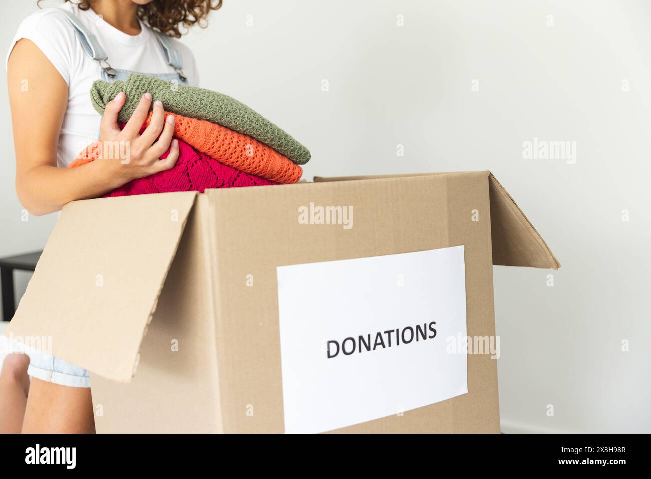 Une jeune femme caucasienne emballant des vêtements dans une boîte de dons à la maison Banque D'Images