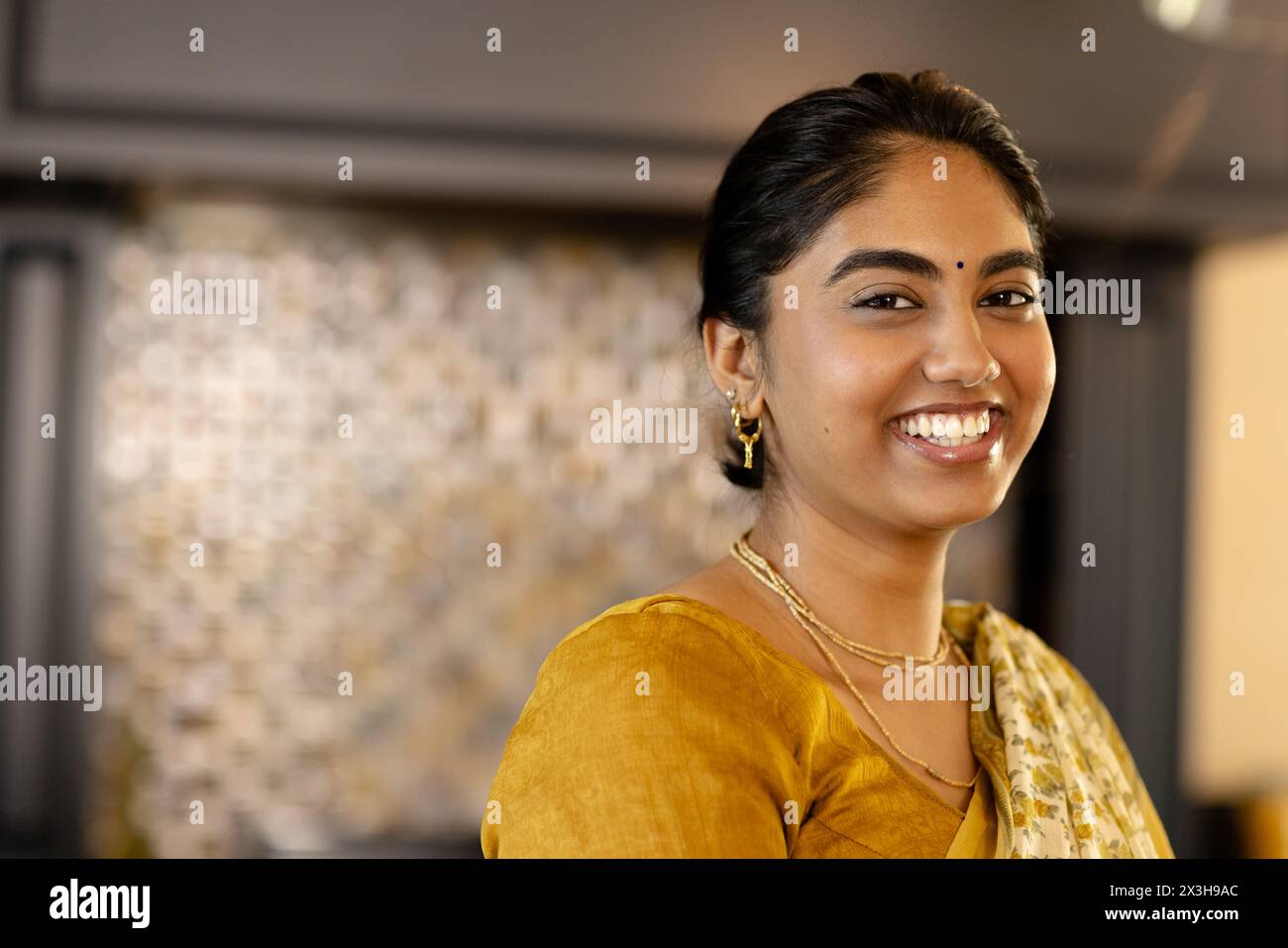 Jeune femme indienne portant une tenue traditionnelle jaune souriante à la maison, espace copie Banque D'Images
