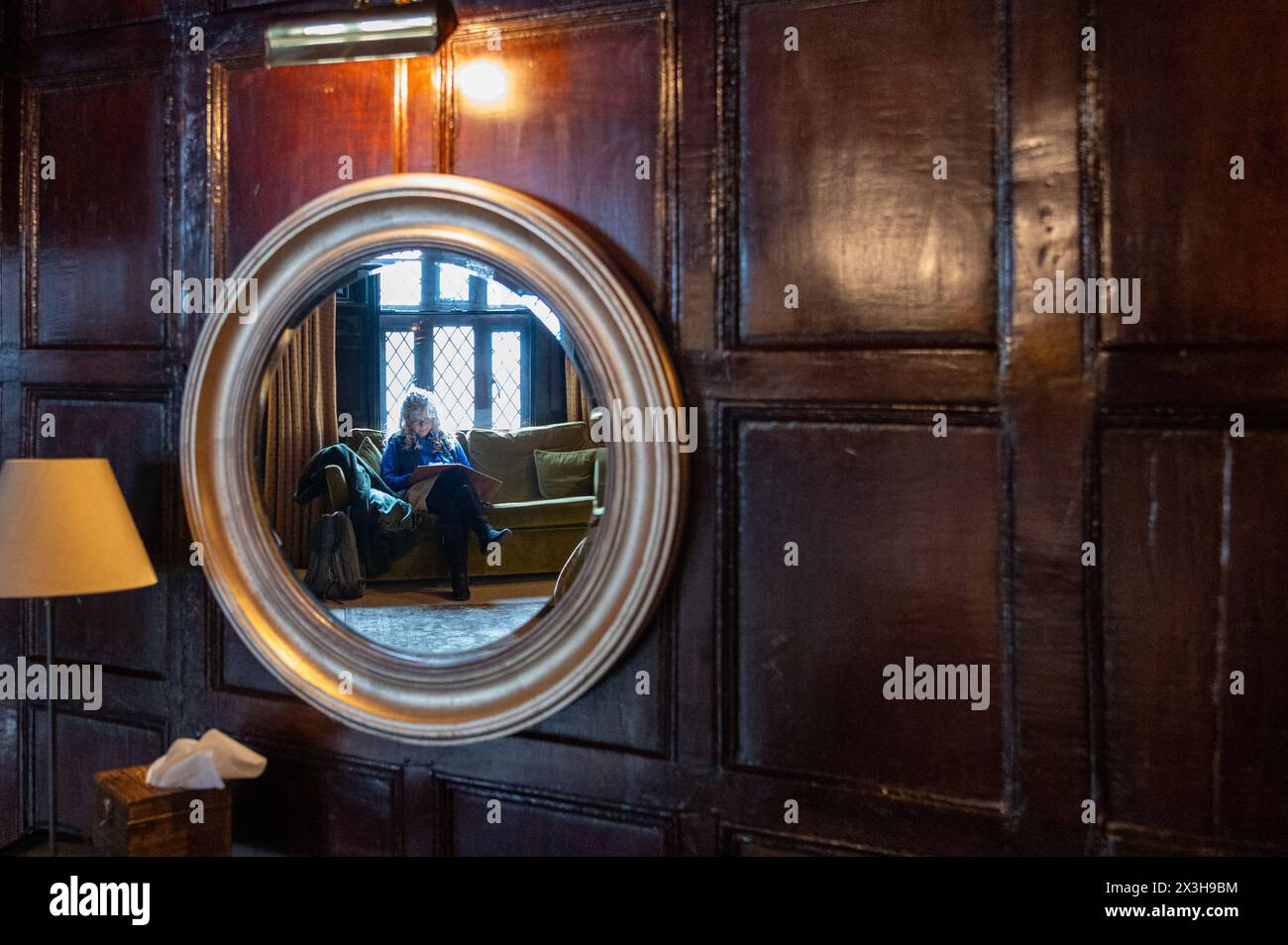 Une femme mystérieuse dans un miroir rond dans une vieille pièce lambrissée de chêne Banque D'Images