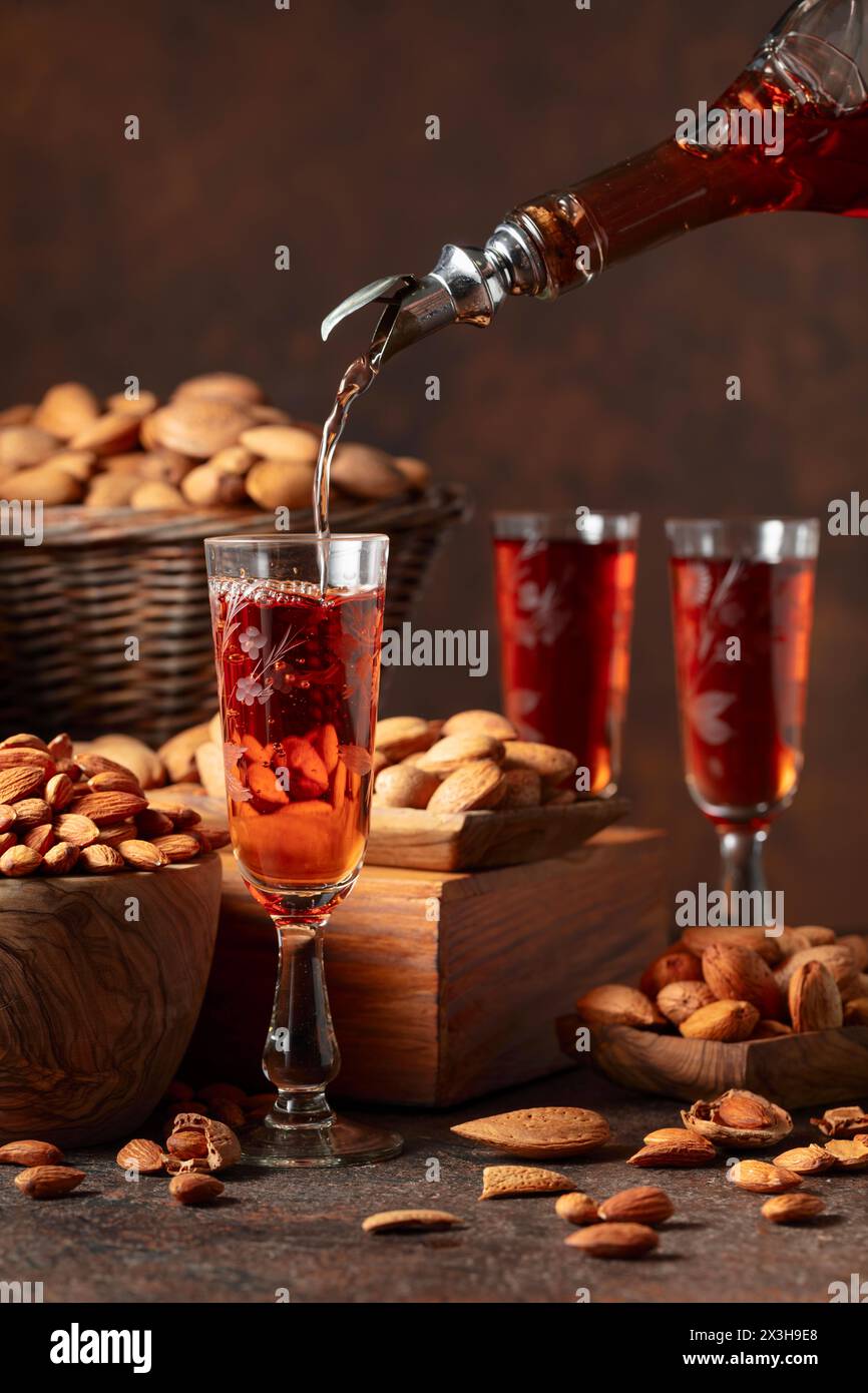 Liqueur italienne Amaretto avec des noix d'amandes sur une table vintage. La liqueur est versée d'une bouteille dans un verre. Banque D'Images