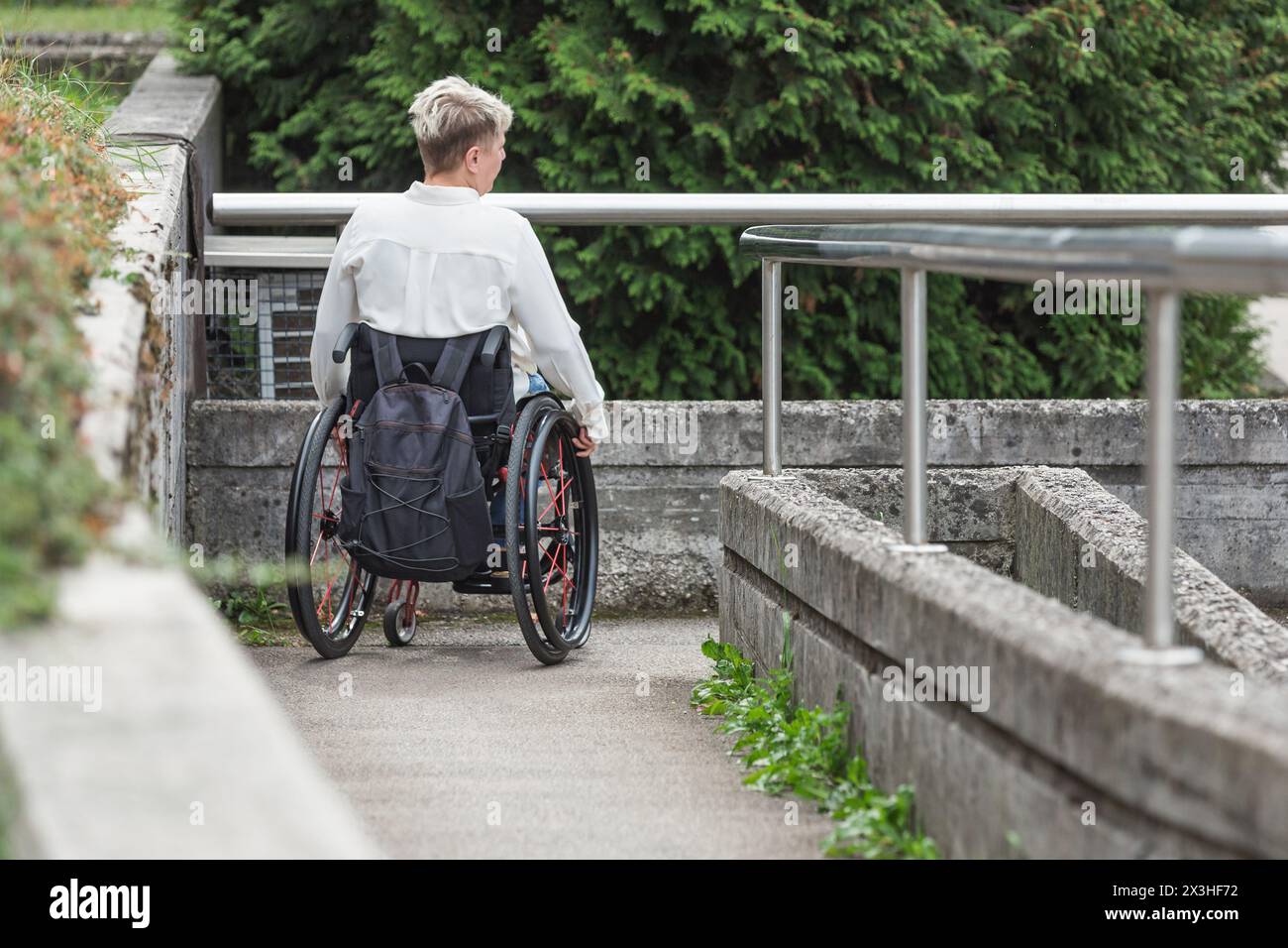 Personne ayant une déficience physique conduisant un fauteuil roulant le long d'une rampe accessible pour accéder à la rue. Handicap et concepts de mobilité. Banque D'Images