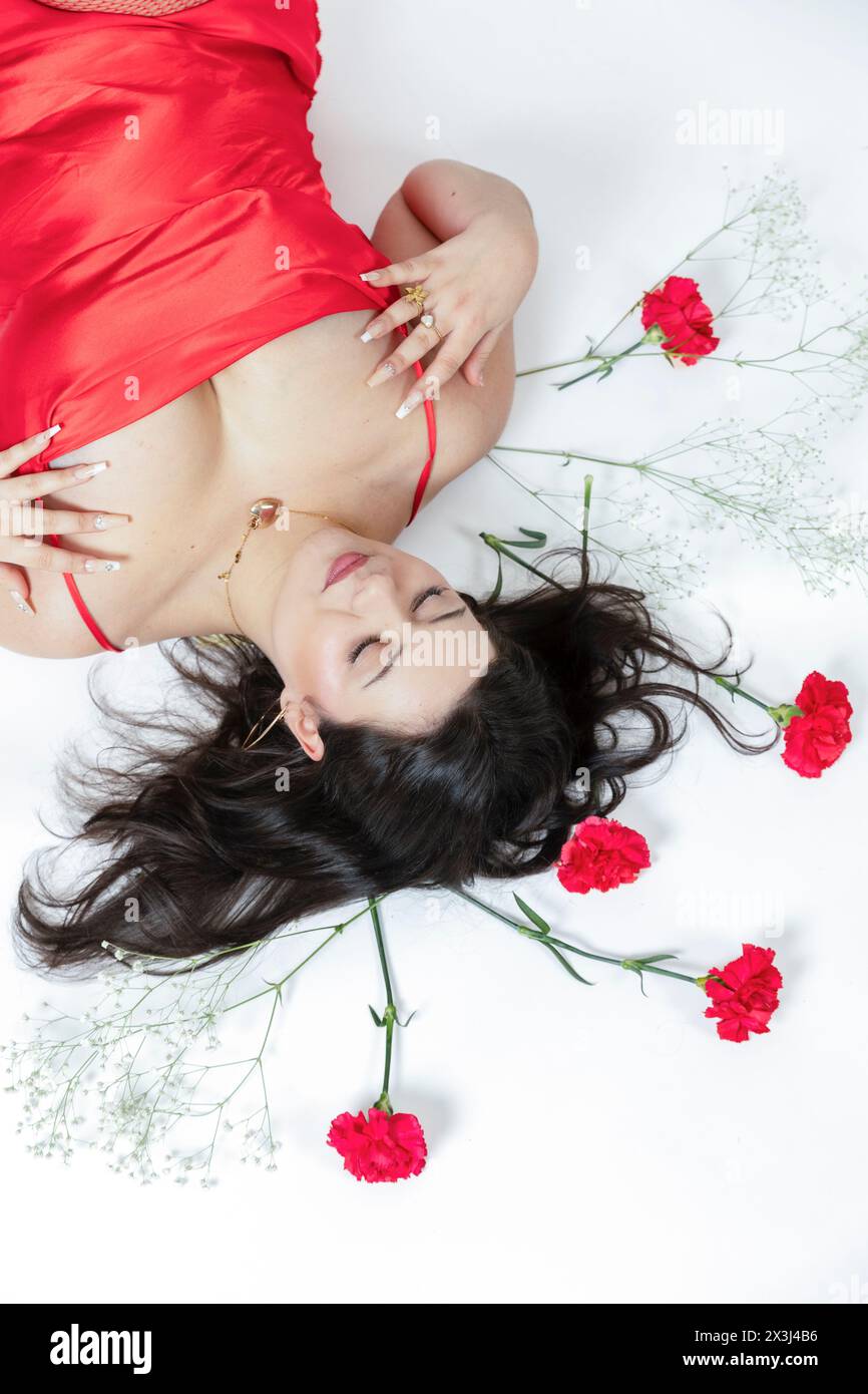 Fille courbée posant avec une robe rouge et quelques fleurs rouges autour d'elle Banque D'Images