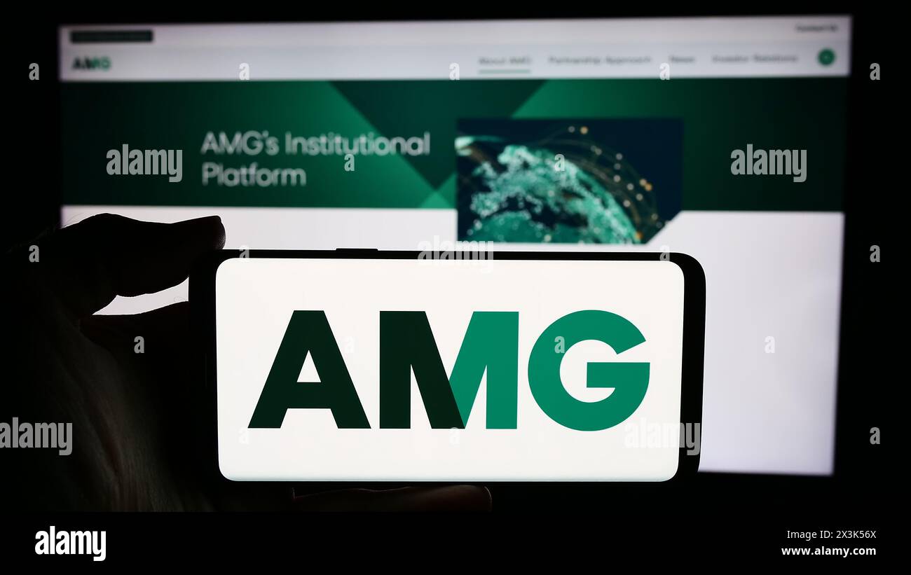 Personne tenant un téléphone portable avec le logo de la société américaine Affiliated Managers Group Inc (AMG) en face de la page Web de l'entreprise. Concentrez-vous sur l'affichage du téléphone. Banque D'Images