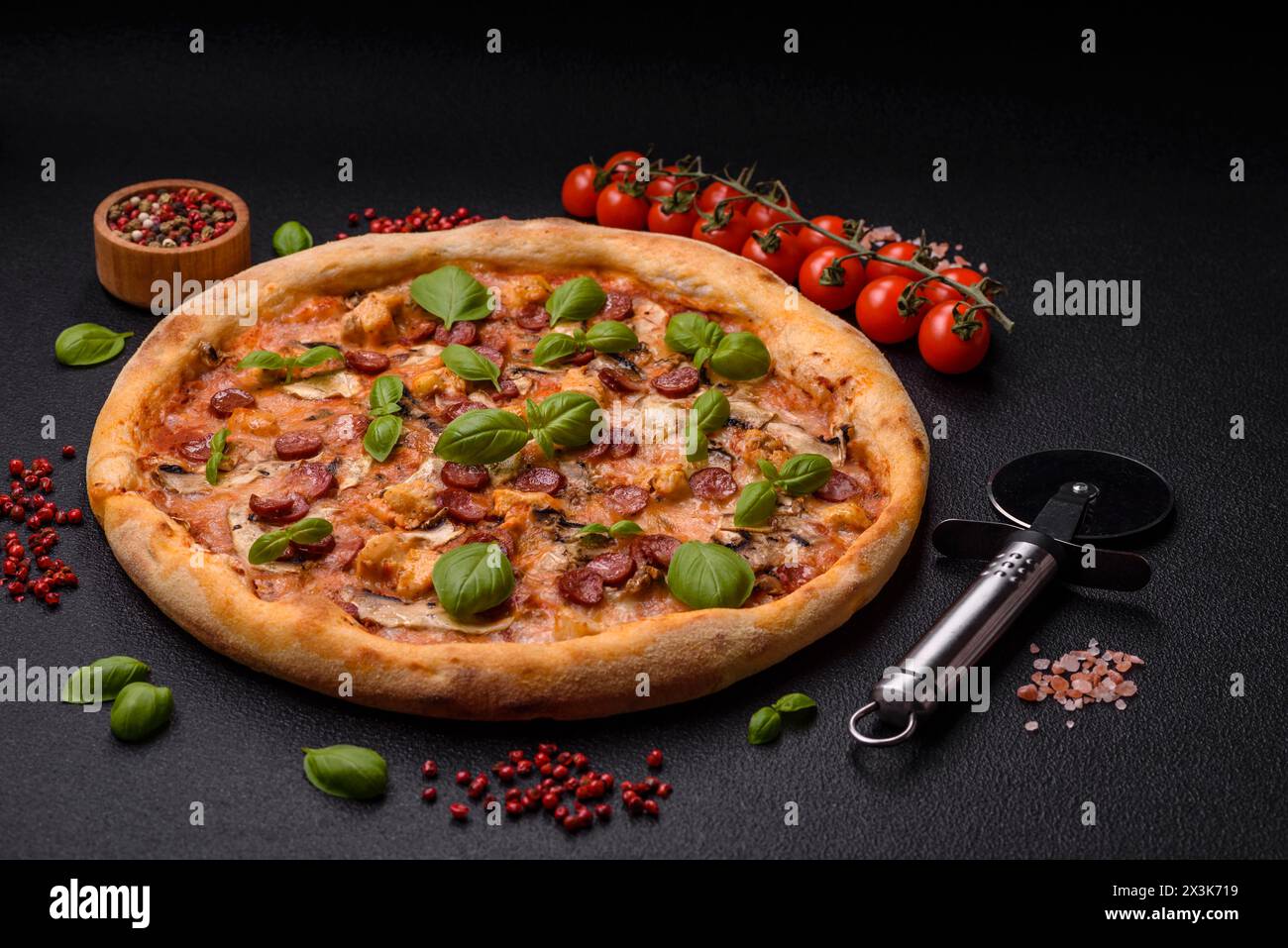 Délicieuse pizza avec saucisse, fromage, tomates, sel, épices et herbes sur un fond de béton foncé Banque D'Images