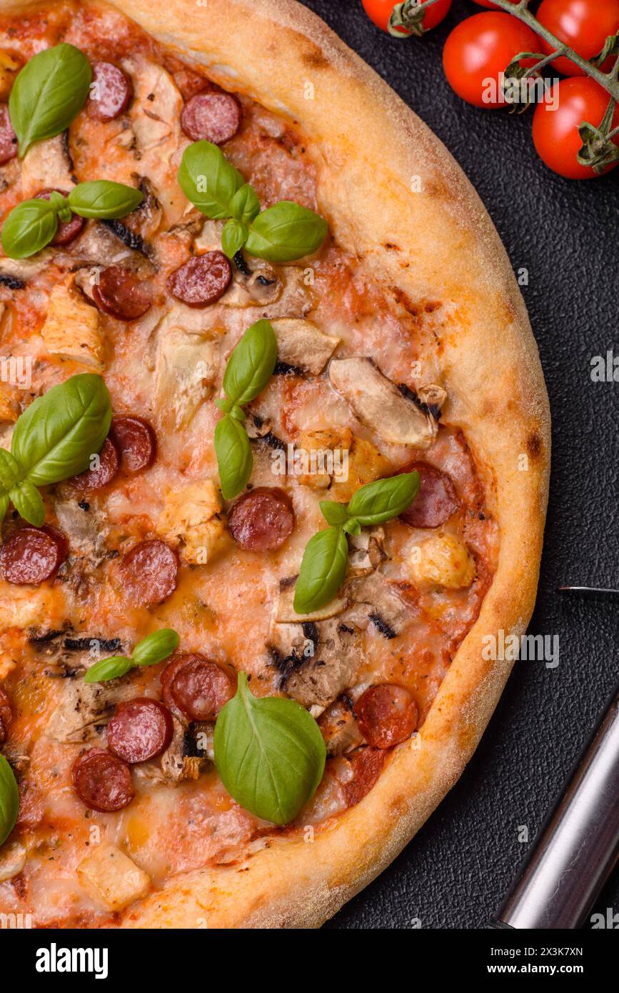 Délicieuse pizza avec saucisse, fromage, tomates, sel, épices et herbes sur un fond de béton foncé Banque D'Images