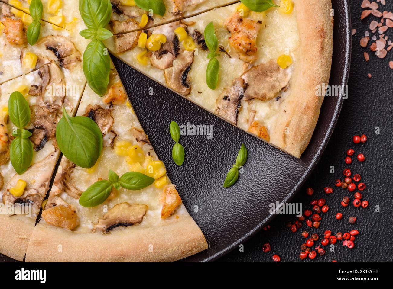 Délicieuse pizza avec du maïs, du fromage, des tomates et des champignons, du sel, des épices et des herbes sur un fond de béton foncé Banque D'Images