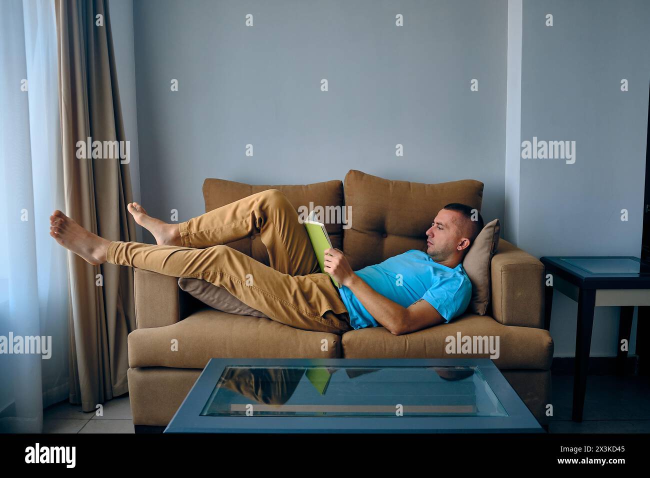 L'homme lit un livre couché sur le canapé Banque D'Images