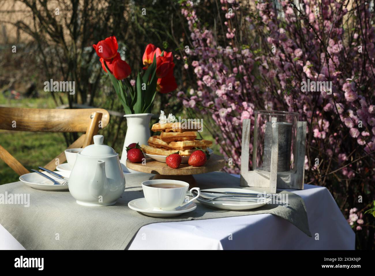 Beau bouquet de tulipes et gaufres fraîchement cuites sur table servi pour boire du thé dans le jardin Banque D'Images