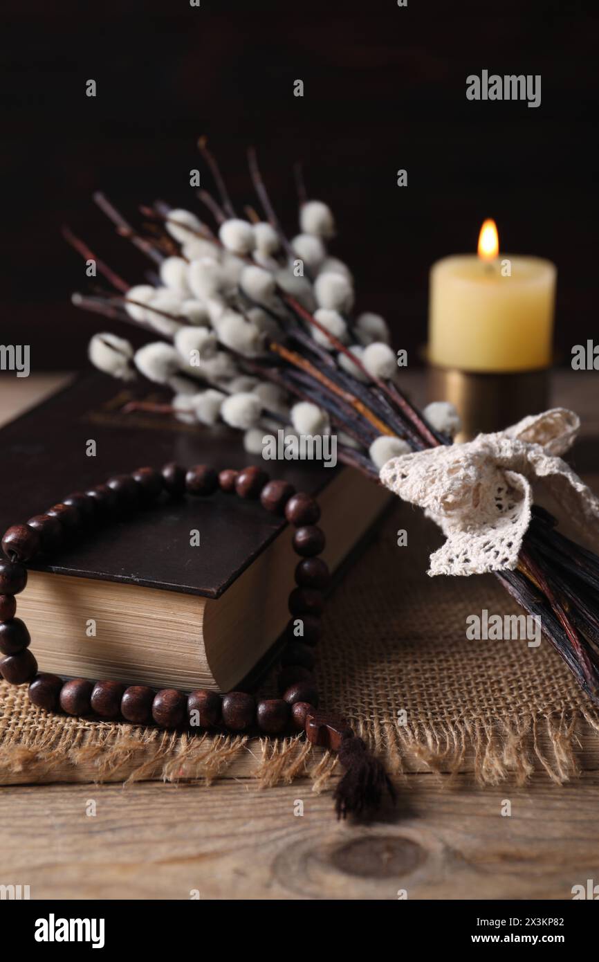 Perles de Rosaire, Bible, bougie allumée et branches de saule sur la table en bois, gros plan Banque D'Images