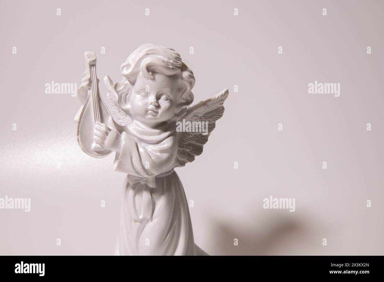Triste sculpture d'ange gardien avec de longues ailes ouvertes à travers le cadre désaturé contre un ciel blanc brillant. La triste sculpture d'expression avec les yeux vers le bas Banque D'Images