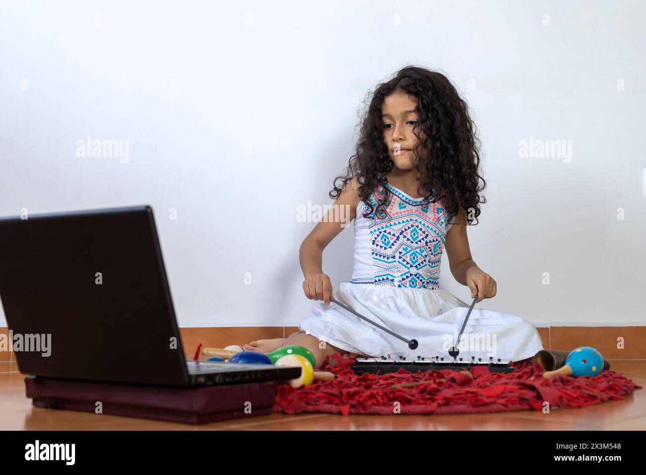 Fille latino-américaine recevant son cours de musique virtuel jouant un xylophone Banque D'Images