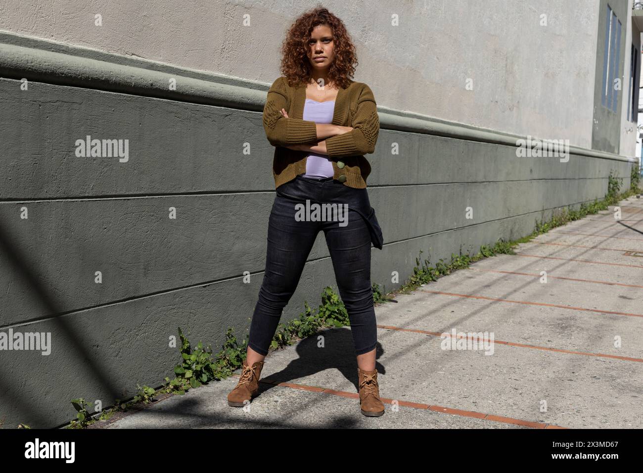 Femme adulte latino-américaine (34) d'ascendance africaine avec les cheveux bouclés pose avec les bras croisés et attitude sérieuse. Concept de style de vie. Banque D'Images