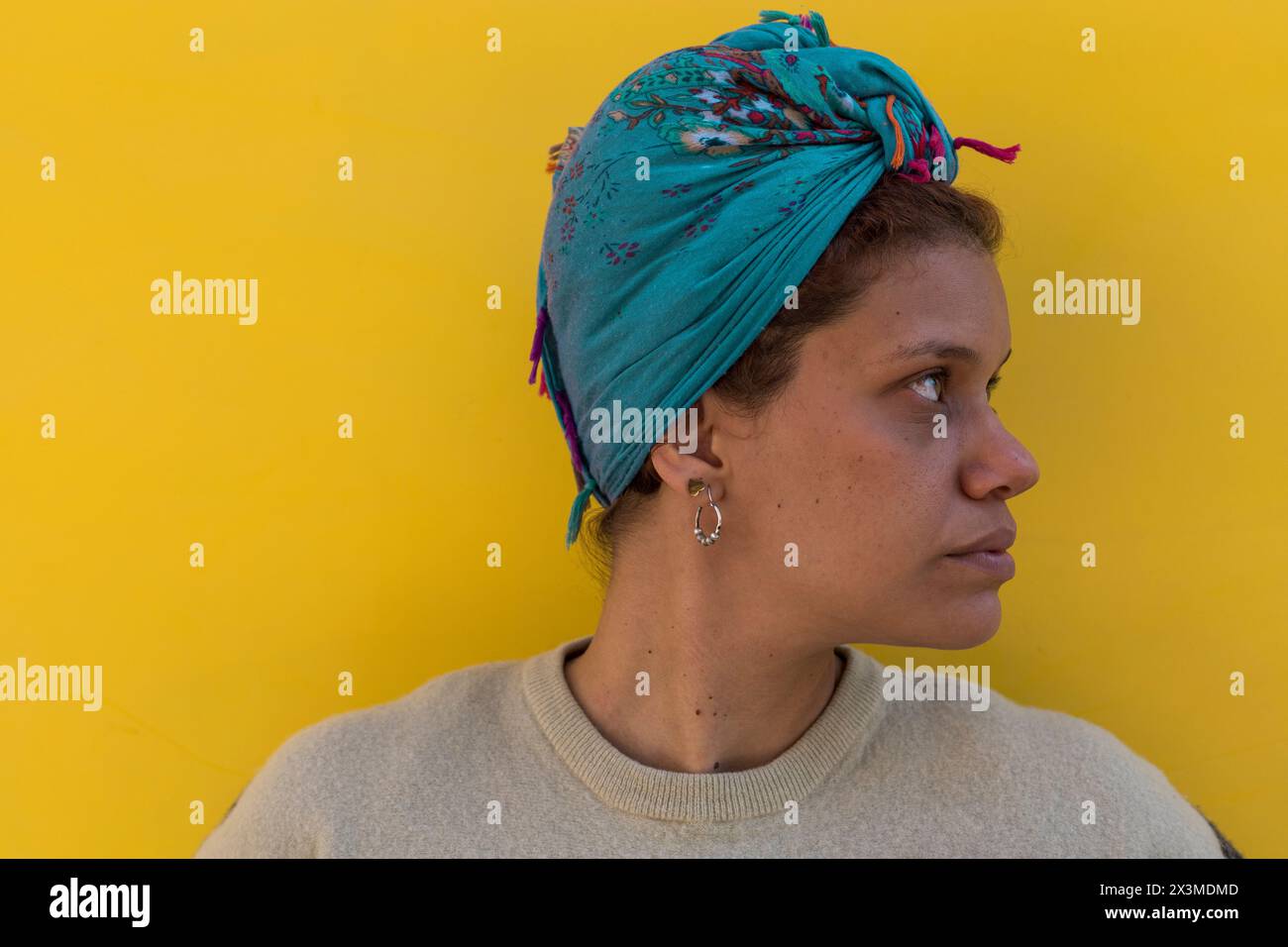 Afro Latino-américaine femme (34) avec les yeux verts, foulard et isolée sur fond jaune avec sa tête tournée vers son côté gauche. Banque D'Images