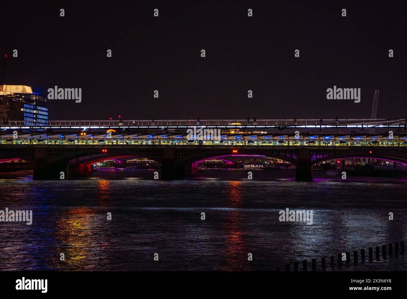 Train de nuit garé sur Blackfriars Bridge à Londres la nuit, avec les lumières violettes reflétant dans l'eau de la Tamise et du Millennium BRI Banque D'Images