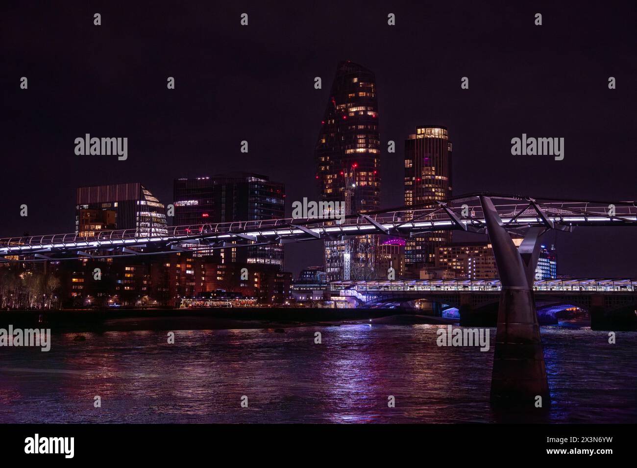 Millennium Bridge illuminé la nuit, avec les lumières violettes reflétant dans l'eau de la Tamise avec des piétons marchant le long de celui-ci et un nig Banque D'Images
