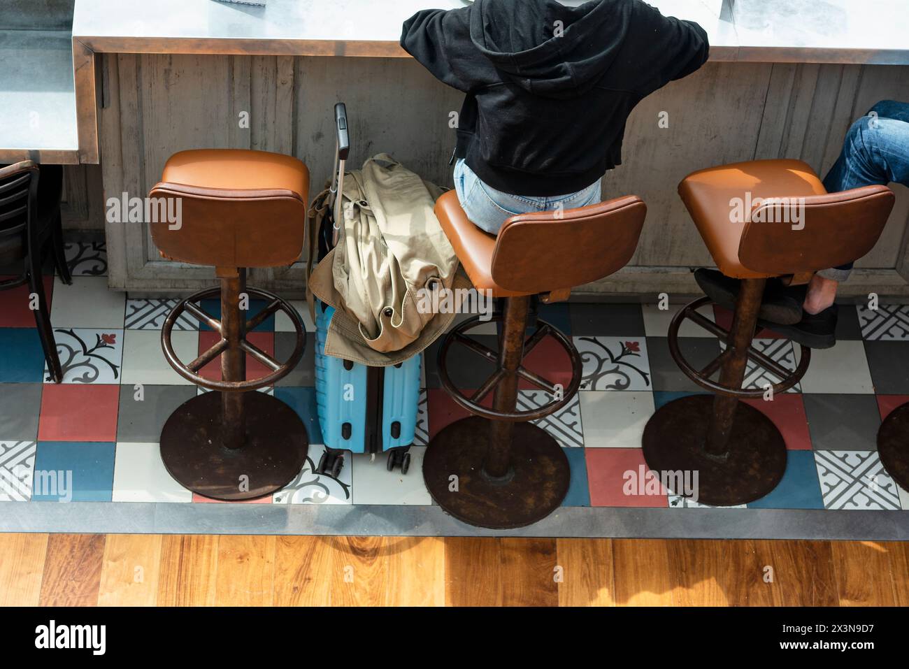 Vue arrière d'une femme assise dans un tabouret de bar, appuyée contre le comptoir en bois, avec son chariot attend le départ de leur vol de CDG airpor Banque D'Images