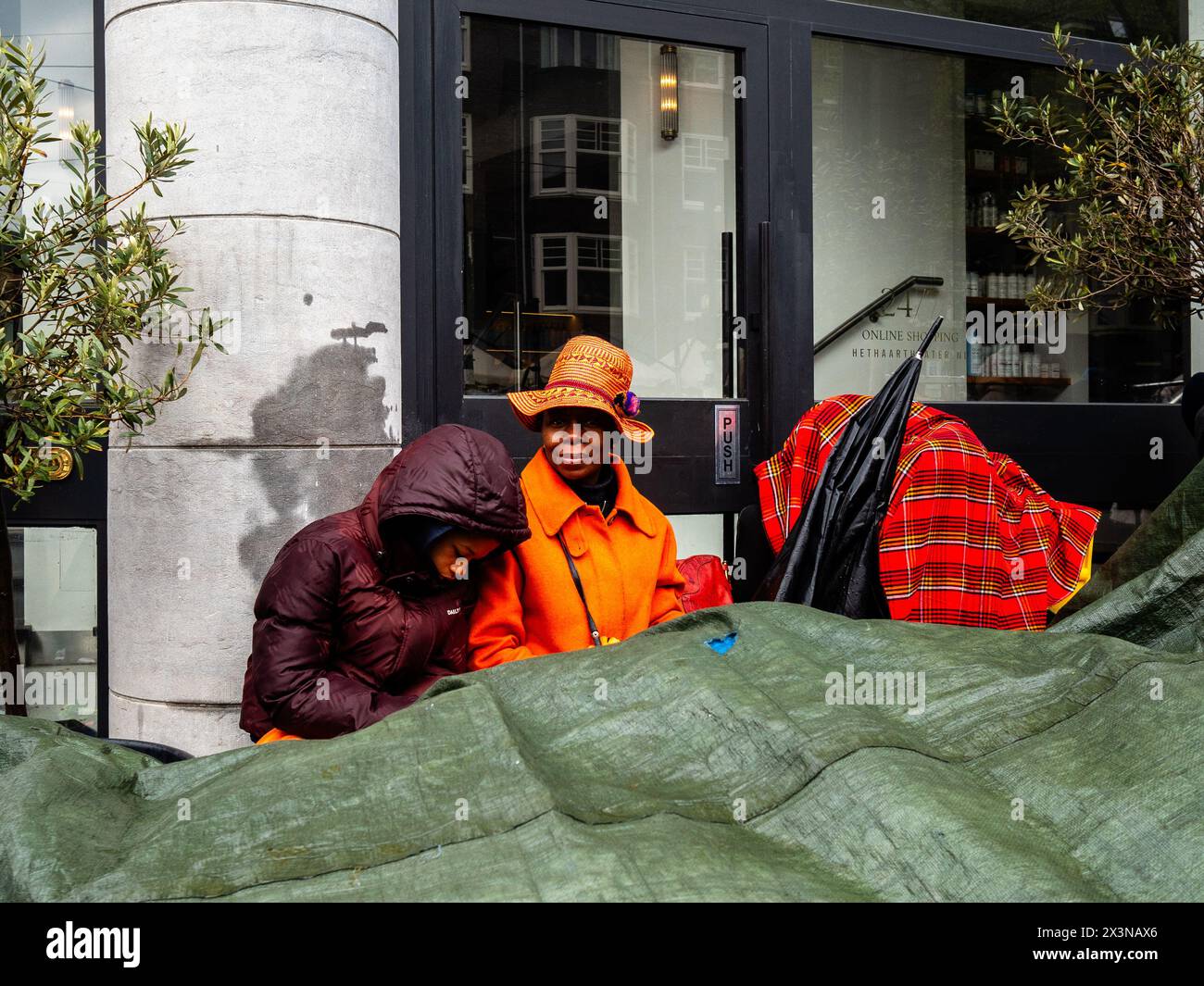 Amsterdam, pays-Bas. 27 avril 2024. Une femme noire et sa fille sont vues couvrant ses affaires à vendre à cause de la pluie. La fête du Roi est réputée pour être l'une des festivités les plus grandes et les plus colorées du pays, en particulier à Amsterdam. La ville regorge d'orange alors que les gens profitent de la plus grande fête de rue de l'année, en profitant des marchés libres et en s'amusant sur les bateaux le long des canaux. Crédit : SOPA images Limited/Alamy Live News Banque D'Images