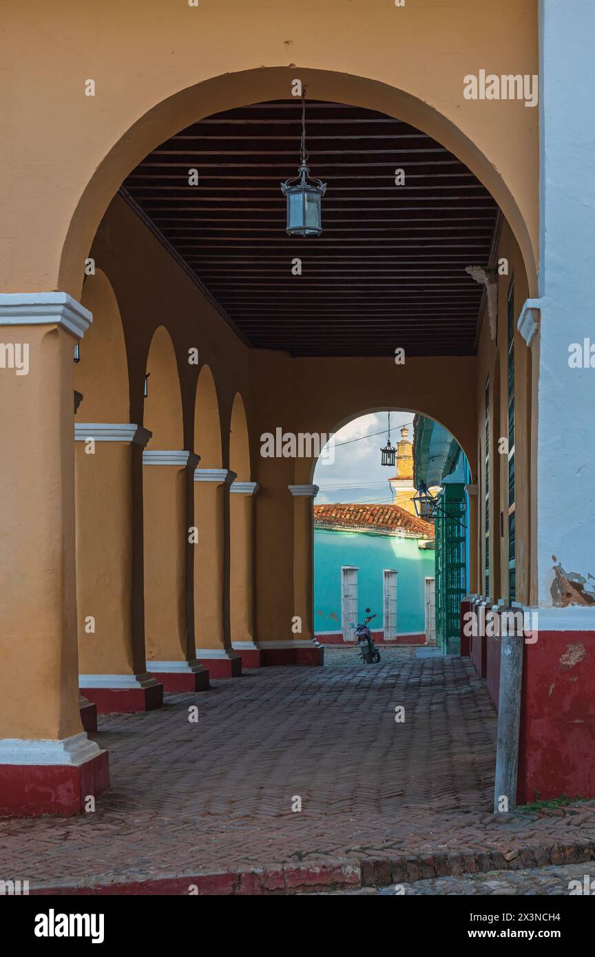 Vue à travers les arches le long de la façade d'un vieux bâtiment coloré avec un pavé de briques dans la vieille ville, Trinidad, Cuba. Banque D'Images