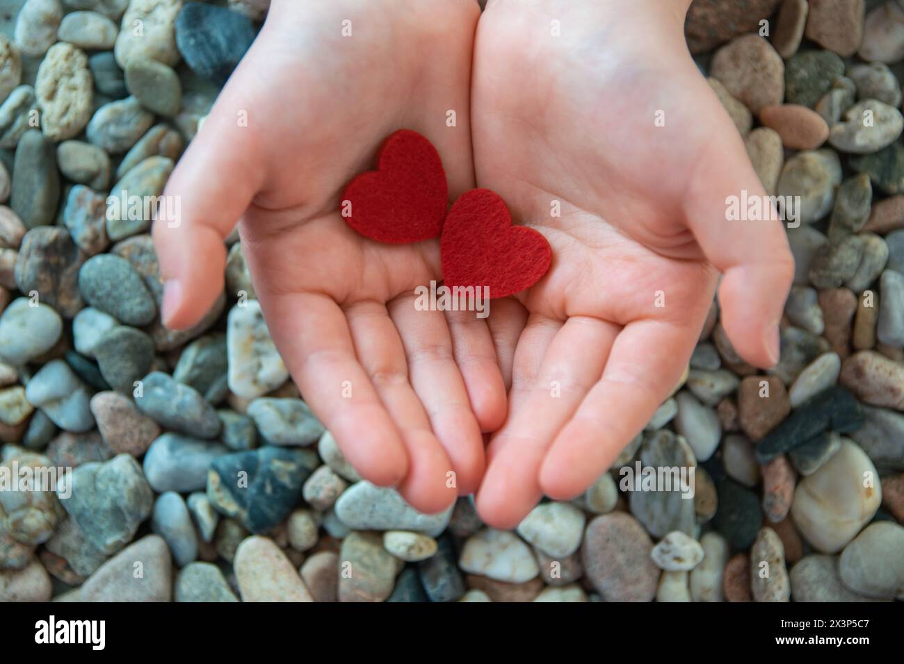 Coeur de tissu rouge dans les mains d'enfant sur le fond de pierres. Concept de Saint Valentin et amour romantique. Banque D'Images