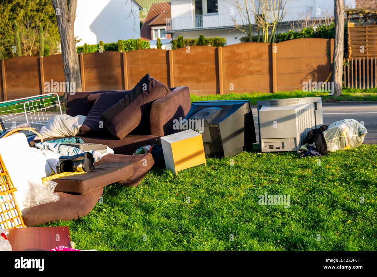 Déchets dans une ville près de la haus. Grandes ordures avec vieux meubles en bois, jouets, boîtes, sacs en plastique dans une rue et l'herbe verte au printemps ensoleillé décharge de déchets d Banque D'Images