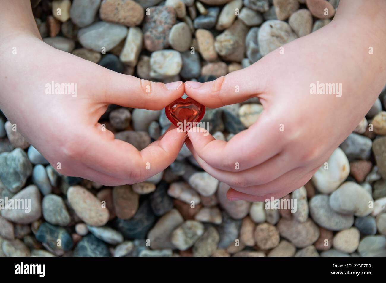 Coeur en verre rouge brillant dans la main de l'enfant sur le fond de pierres. Concept de Saint Valentin et amour romantique. Banque D'Images