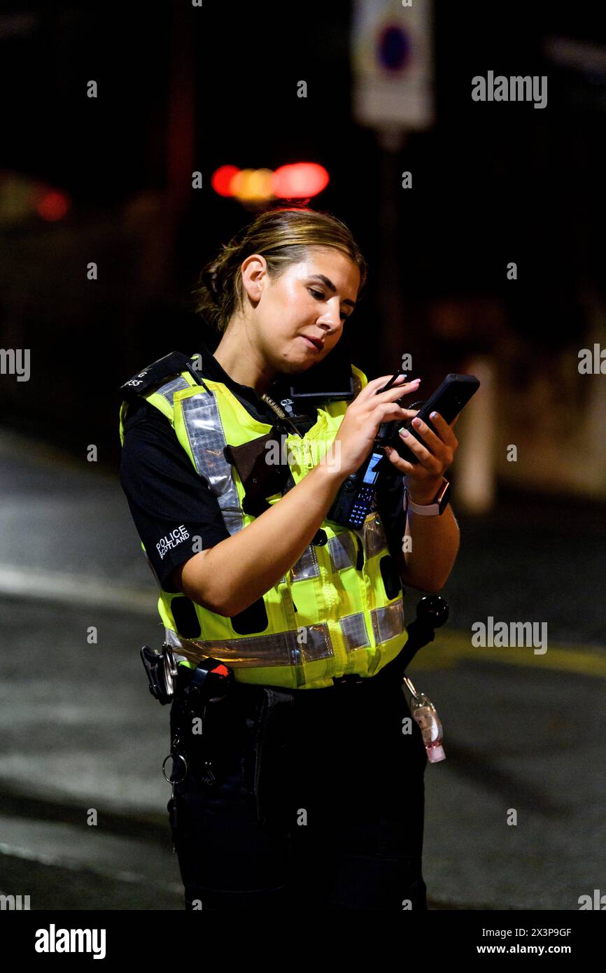Une officière de Police Scotland vérifie son téléphone et sa radio lors d'une patrouille de nuit à Glasgow, Écosse, Royaume-Uni Banque D'Images