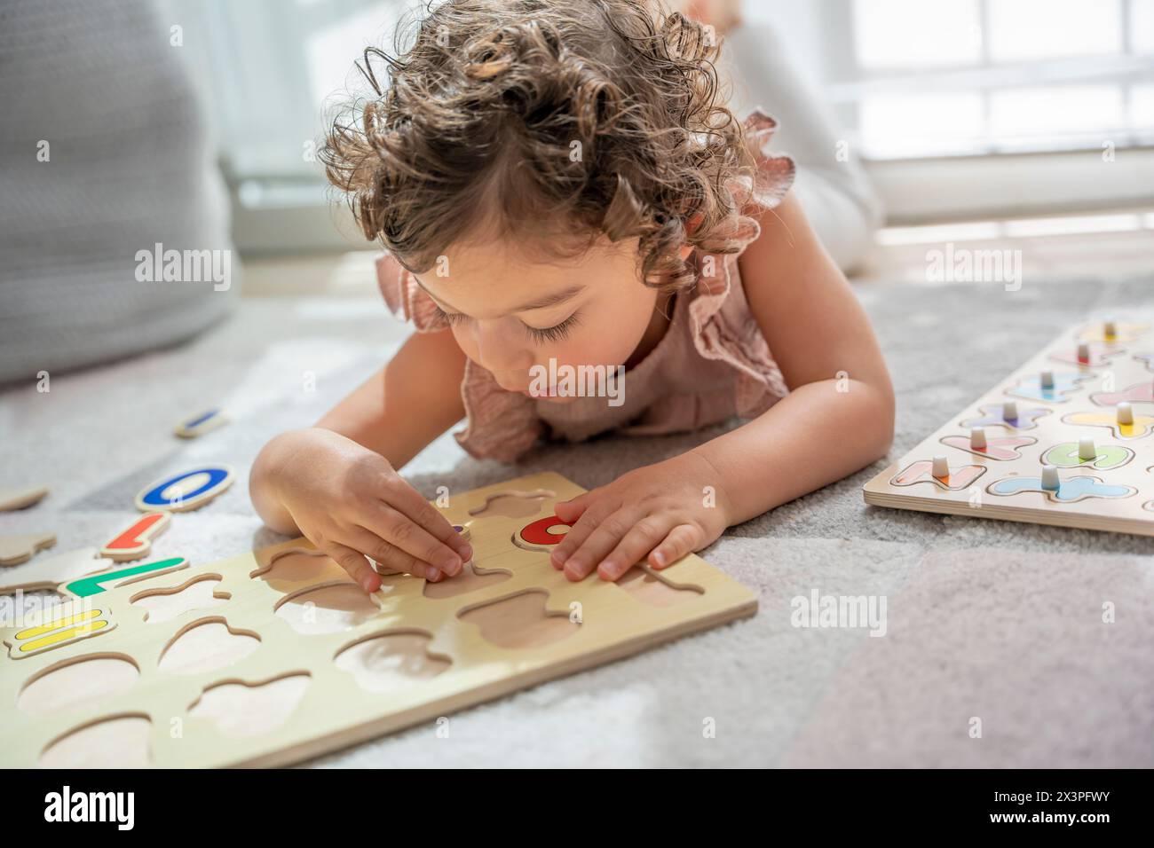 Image en gros plan d'une petite fille allongée sur un tapis de jeu jouant avec un puzzle en bois de lettre alphabet. Méthodologie Montessori et matériaux. education, dev Banque D'Images