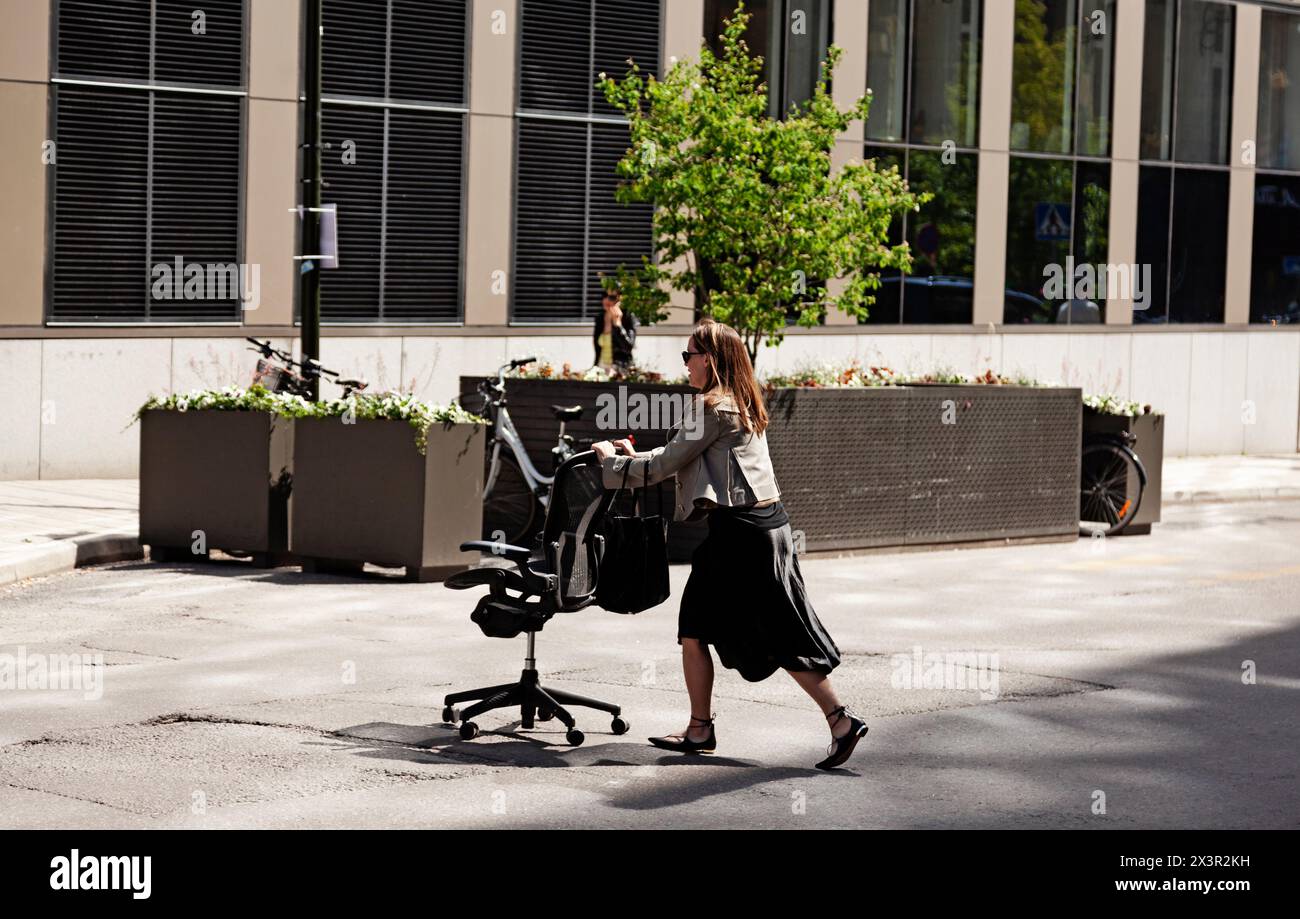 Stockholm, Suède - 23 mai 2023 : femme poussant une chaise de bureau de l'autre côté de la rue vers une autre maison Banque D'Images