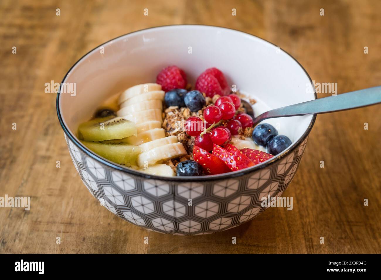 Bol de yaourt frais (yaourt) avec granola, baies d'été mélangées, banane et kiwi avec une cuillère sur une table en bois Banque D'Images