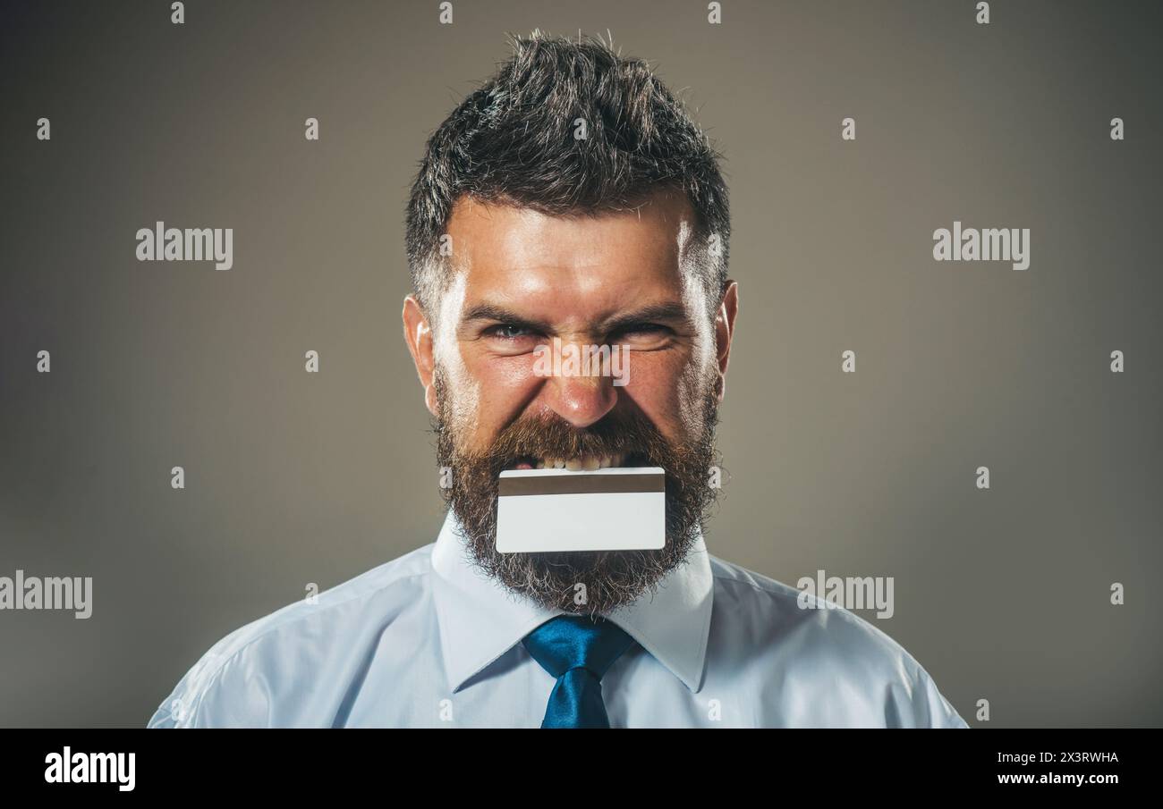 Bel homme barbu en chemise blanche et cravate bleue avec carte de crédit dans les dents. Services bancaires publicitaires, prêts ou dépôts, cashback pour les achats Banque D'Images