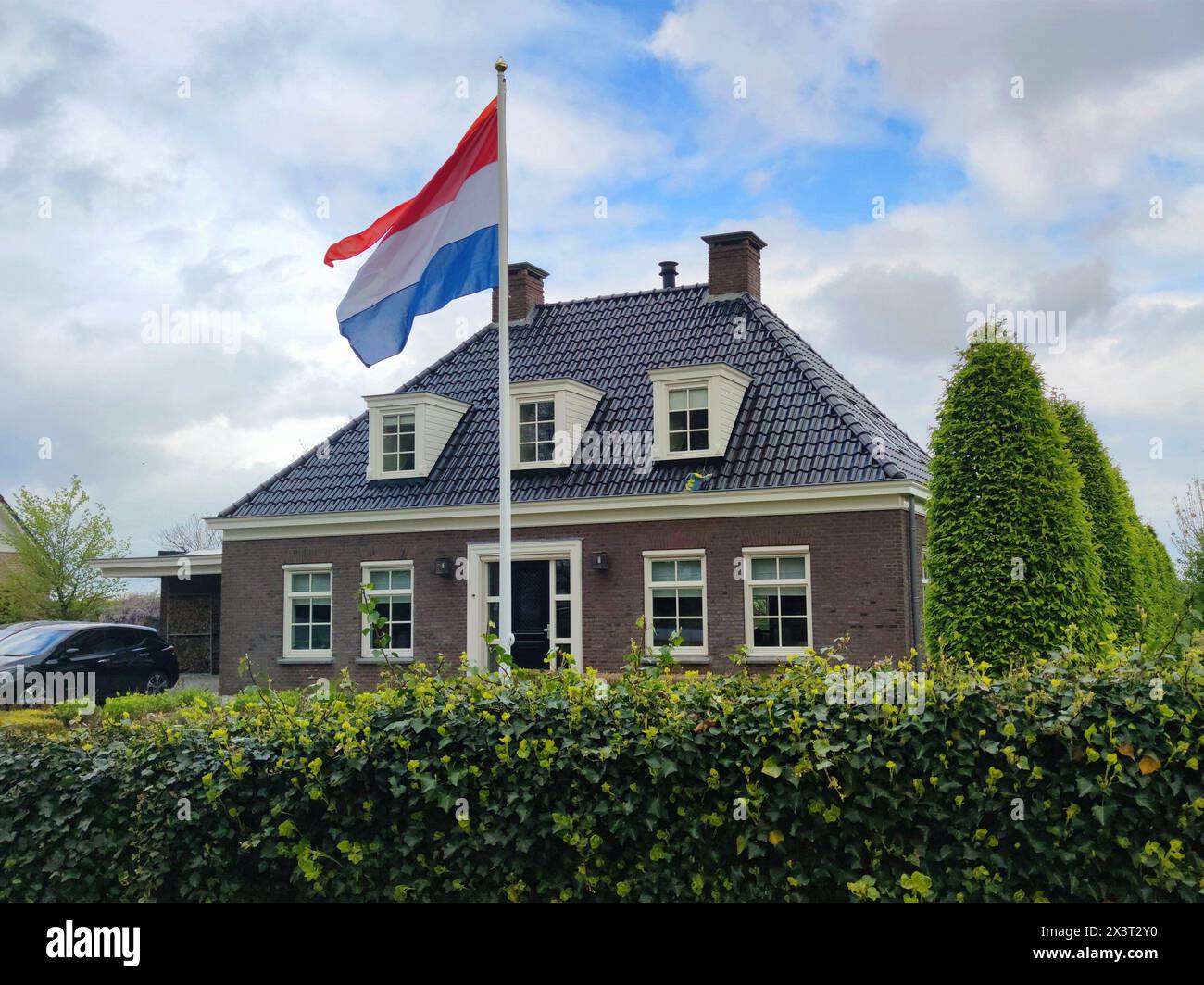 Drapeau hollandais flottant devant une maison nouvellement construite ¨style cottage¨ sur la fête nationale néerlandaise ¨Koningsdag¨ (jour des rois). Banque D'Images