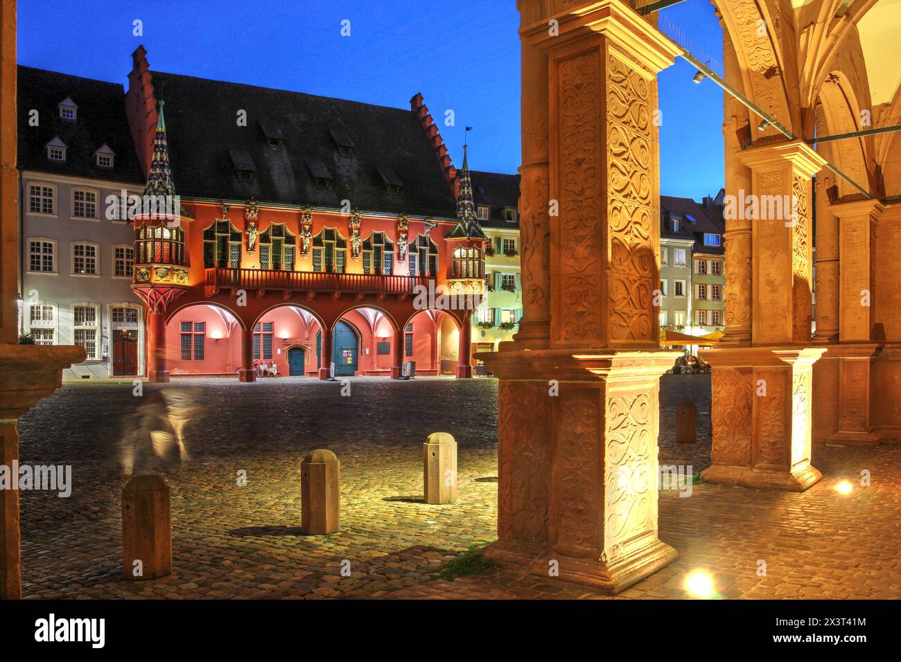 Scène de nuit sur la place Minster, Freiburg im Breisgau, Allemagne captivant la salle rouge frappante des marchands historiques (Historisches Kaufhaus). Banque D'Images