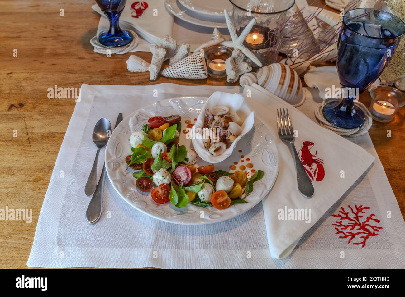 Mélange de fruits de mer et salade Caprese avec tomates cerises, mozzarella, basilic et roquette sur une belle assiette avec une table décorée en coquillage. Banque D'Images