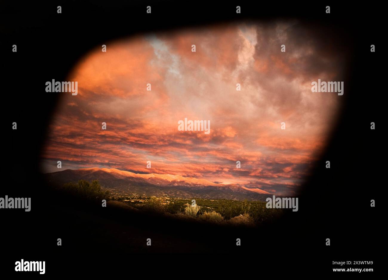 Un coucher de soleil néo-mexicain coloré se reflète dans le rétroviseur latéral d'une voiture, révélant les montagnes Sangre de Cristo enneigées. Banque D'Images