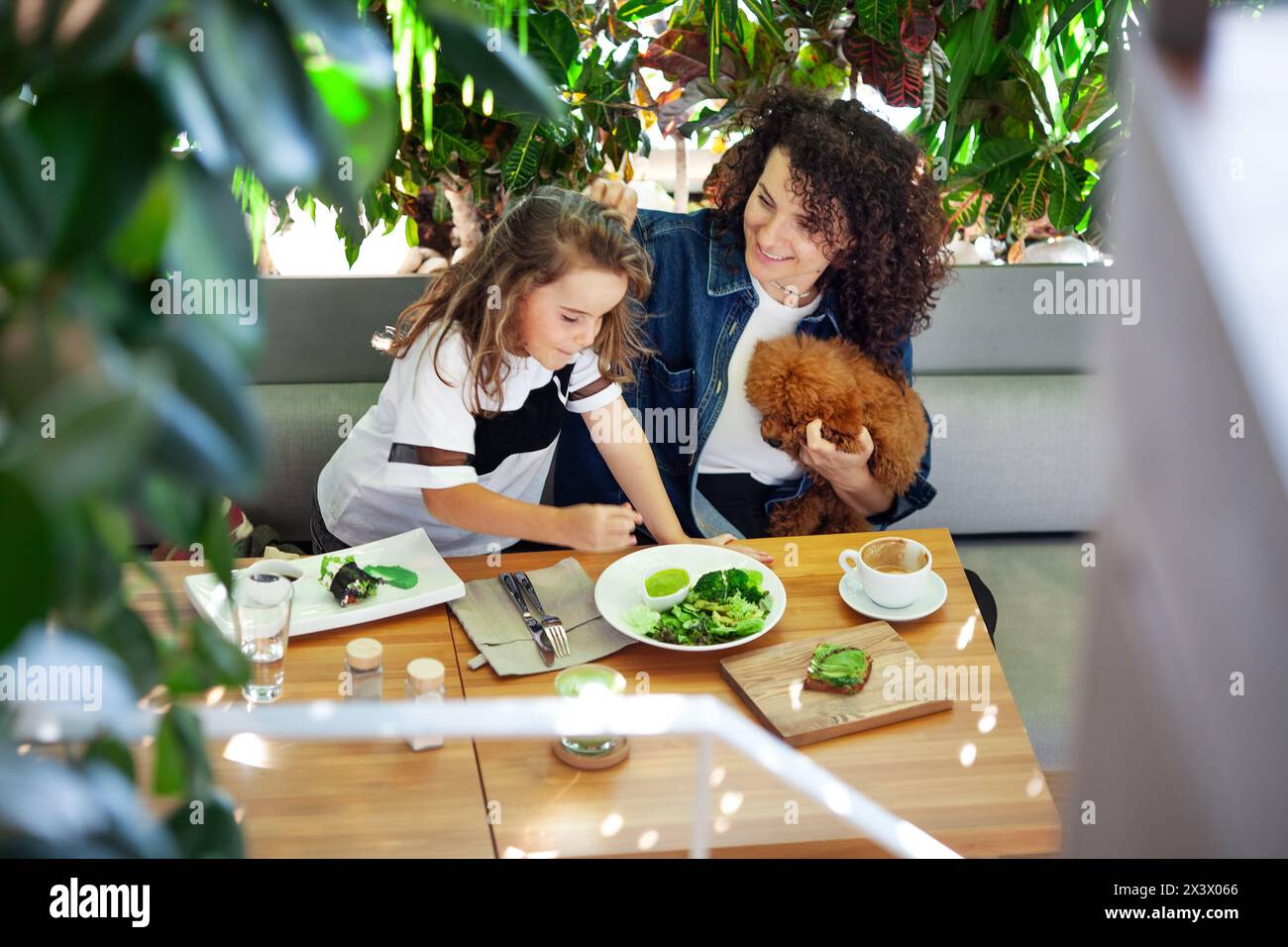 Une femme et une fille sont assises à une table, dégustant un repas de légumes ensemble. Divers plats et ustensiles sont étalés sur la table au fur et à mesure qu'ils s'engagent Banque D'Images