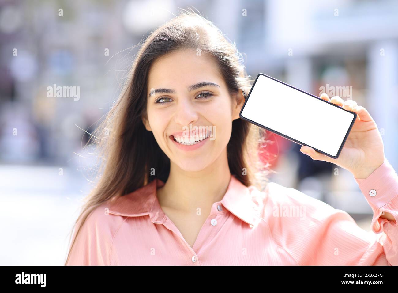 Portrait de vue de face d'une femme heureuse élégante montrant l'écran de téléphone vierge dans la rue Banque D'Images