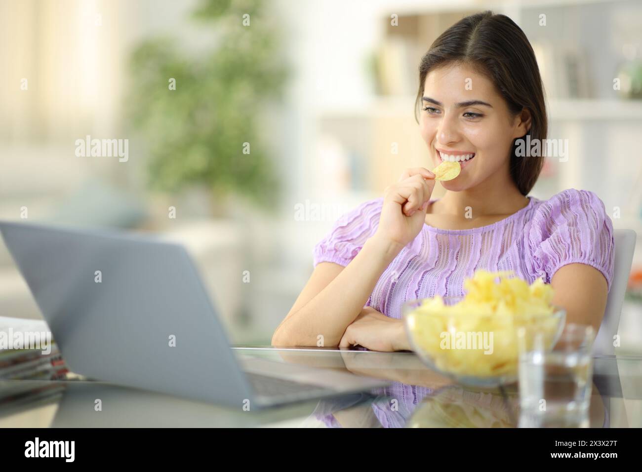 Femme heureuse mangeant des croustilles regardant les médias sur ordinateur portable à la maison Banque D'Images