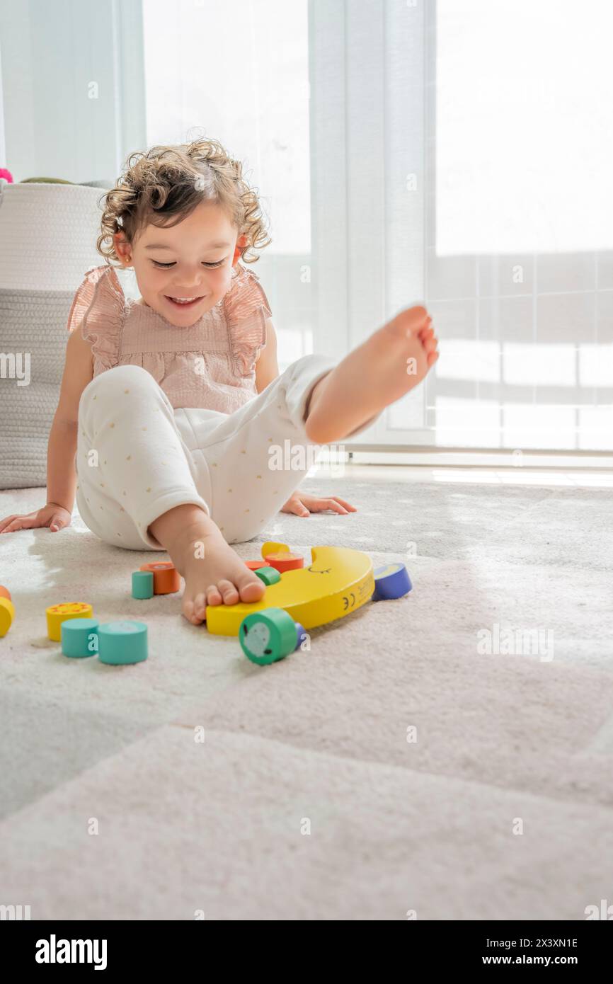 Photographie verticale d'une fille souriante tout en s'amusant à jouer avec des morceaux de bois durable coloré. matériaux montessori. développement et apprentissage Banque D'Images