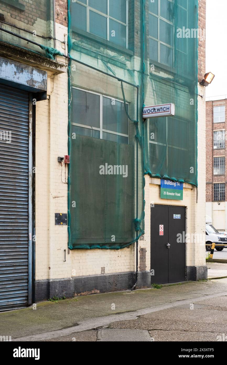 Photographie d'un bâtiment industriel avec un filet vert à travers les fenêtres, une double porte en bas à droite, un volet fermé à gauche et un ancien Banque D'Images