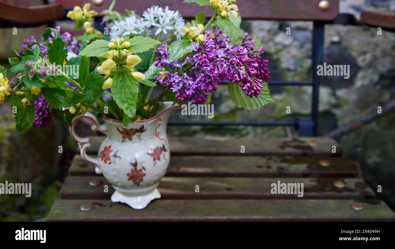 Fleurs de jardin dans une vieille cruche à lait sur une chaise de jardin. Banque D'Images