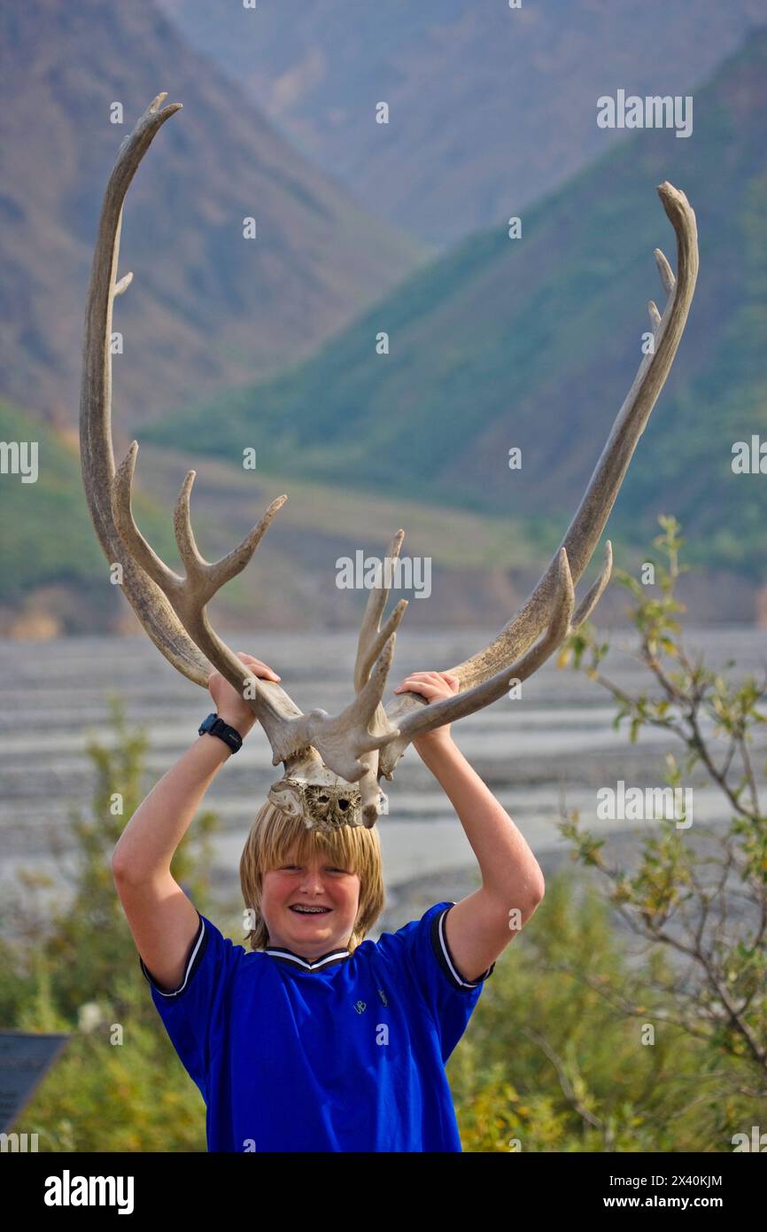 Boy essaie une paire d'énormes bois de caribou dans le parc national et la réserve Denali ; Alaska, États-Unis d'Amérique Banque D'Images