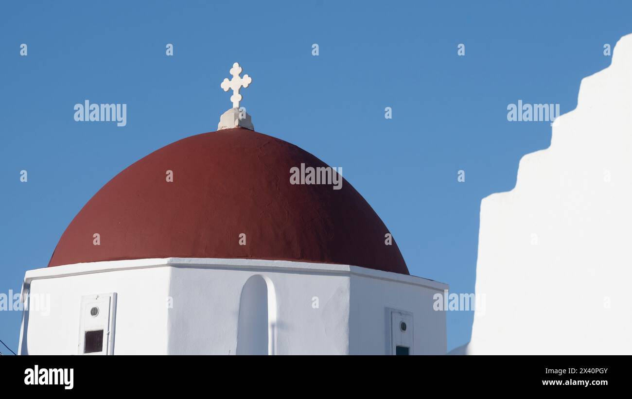 Croix et dôme rouge sur une église blanchie contre un ciel bleu vif sur l'île de Mykonos ; Mykonos, sud de la mer Égée, Grèce Banque D'Images