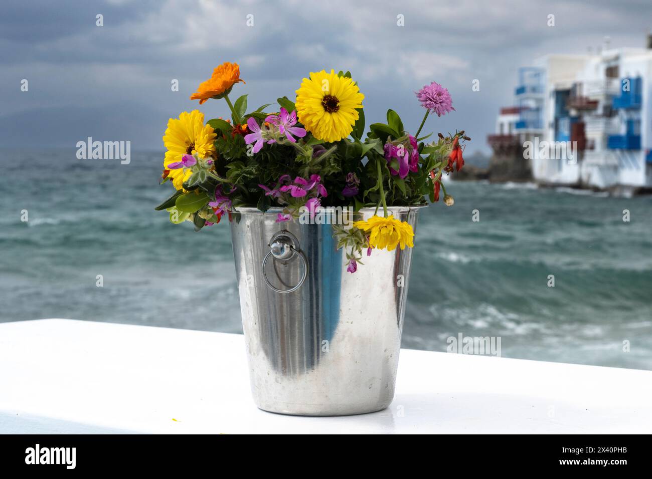 Seau de fleurs coupées sur un mur blanchi à la chaux avec logement en bord de mer en arrière-plan sur l'île de Mykonos en Grèce ; Mykonos, Grèce Banque D'Images