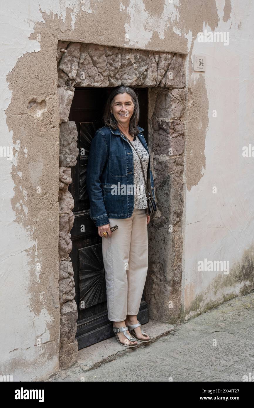 Femme debout dans une porte en pierre basse qui correspond à sa taille, sur l'île de Sardaigne en Italie ; Castelsardo, Sassari, Italie Banque D'Images