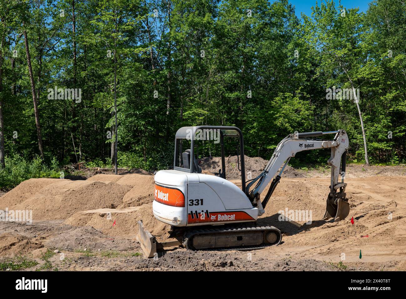CROW WING CO, MN - 6 juin 2021 : une mini-pelle Bobcat 331, avec des chenilles de direction à glissement, est assise sur la terre à un terrain de construction vide bordé d'arbres, en préparation f Banque D'Images
