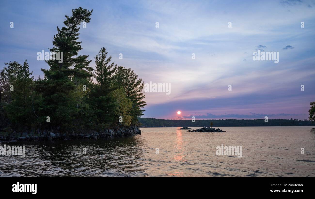 Coucher de soleil pittoresque sur un lac avec un rayon de soleil rose reflété sur l'eau tranquille ; Lac des bois, Ontario, Canada Banque D'Images