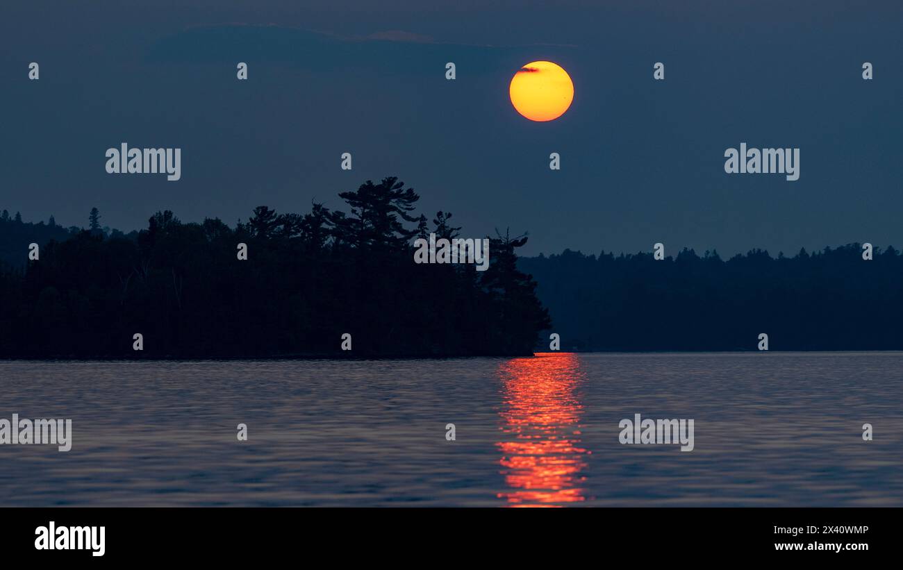 Coucher de soleil brillant sur un lac avec des arbres silhouettes le long du rivage et un rayon de soleil réfléchi sur la surface de l'eau Banque D'Images