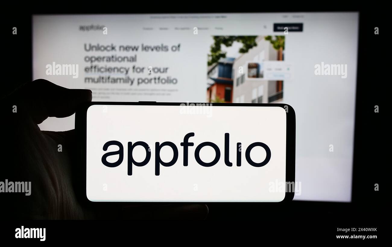 Personne tenant le téléphone portable avec le logo de la société américaine de logiciels immobiliers AppFolio Inc. en face de la page Web de l'entreprise. Concentrez-vous sur l'affichage du téléphone. Banque D'Images