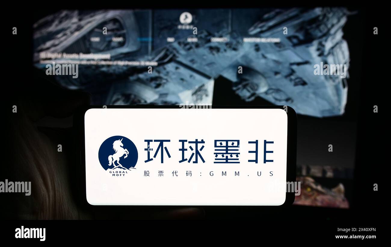 Personne tenant le téléphone portable avec le logo de la société chinoise Global Mofy Metaverse Limited en face de la page Web de l'entreprise. Concentrez-vous sur l'affichage du téléphone. Banque D'Images